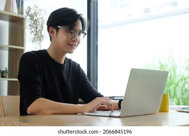 Smiling Asian Man Working With Laptop Computer At Home Office.