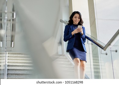 Smiling Asian manager in formalwear texting with friend on smartphone while going downstairs, portrait shot - Powered by Shutterstock