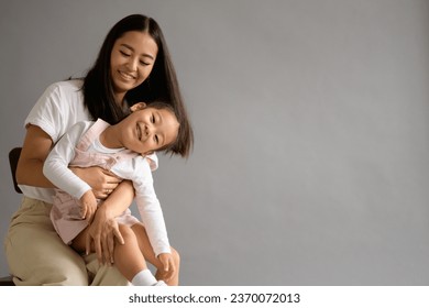 Smiling asian mom hugging toddler daughter isolated on grey background	 - Shutterstock ID 2370072013