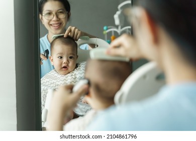 Smiling Asian Mother cutting and trimming her little baby boy hair at home.