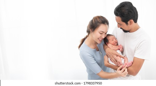 Smiling Asian Mother And Father Holding Their Newborn Baby Son At Home. Proud Asia Mother And Father With Daughter Infant On White Background Banner.