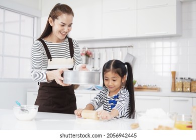 Smiling Asian Mother And Little Asian Girl Child Is Kneading The Dough For Baking Bakery On Wooden Table Together In Kitchen. Homemade Pastry For Bread. Family Love And Homeschool Concept.