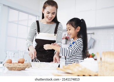 Smiling Asian mother and little asian girl child is Kneading the dough for baking bakery on wooden table together in kitchen. Homemade pastry for bread. Family love and Homeschool Concept.