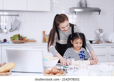 Smiling Asian mother and little asian girl child is Kneading the dough for baking bakery on wooden table together in kitchen. Homemade pastry for bread. Family love and Homeschool Concept.