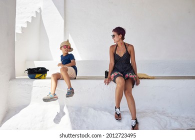 Smiling Asian Mother And Teenage Son Sitting And Relaxing In White Church When Traveling On Island Of Folegandros, Aegean Sea, Greece