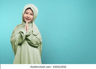 Smiling Asian Muslim Child With Hijab Dress Praying To Over Blue Background