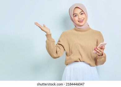 Smiling Asian muslim woman in brown sweater and hijab using a mobile phone, showing copy space on hands isolated over white background. People religious lifestyle concept - Powered by Shutterstock