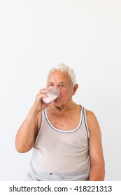 Smiling Asian Old Man In Undershirt Drinking Milk On Blank Background.