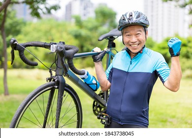 Smiling asian old man is wearing helmet and holding a bicycle then making fist gesture - looking to you