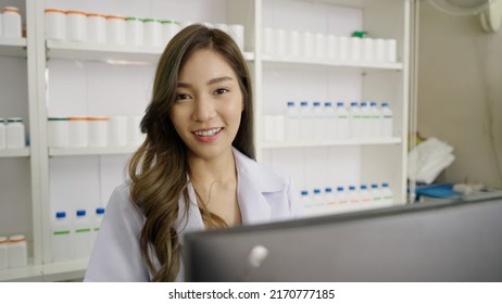 Smiling Asian Pharmacist In Drugstore Or Pharmacy Using Computer And Looking At Camera