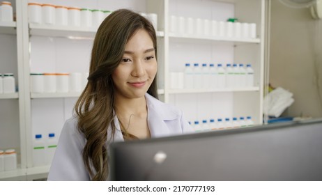 Smiling Asian Pharmacist In Drugstore Or Pharmacy Using Computer