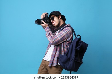 A smiling Asian photographer man is taking images photo with DSLR camera isolated studio blue background. - Powered by Shutterstock