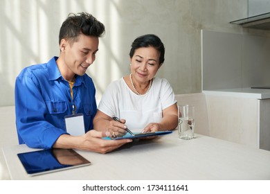 Smiling Asian Service Worker Helping Senior Woman To Sign Contract