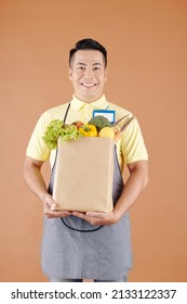 Smiling Asian Supermarket Worker Holding Paper Bag Full Of Fresh Groceries, Fruits And Vegetables