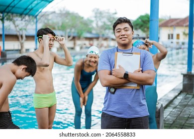 a smiling asian swimming trainer holding a clipboard and stopwatch - Powered by Shutterstock