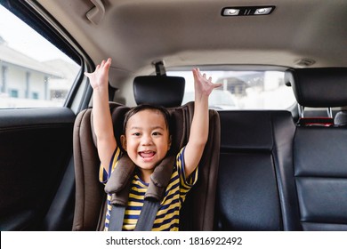 Smiling asian toddler boy raised hand and happy for safe trip on the road.Sitting and buckle up in the car in the seat for children.Coronavirus covid19. Kid boy child in Booster seat exciting for trip