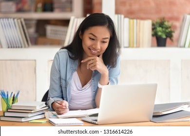 Lächeln asianischer Studierende, Jugendstudierende in der Bibliothek mit Laptop-Büchern, die Online-Forschung für Kurse, machen Hinweise für Essay-Hausaufgaben, Online-Bildung e-Learning-Konzept