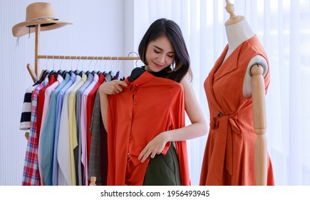 Smiling Asian woman Choose and try on clothe orange color in the Tailor shop. Fashion designer standing in clothing In order to repair, service for customers. Concept Profession Dressmaker designer - Powered by Shutterstock