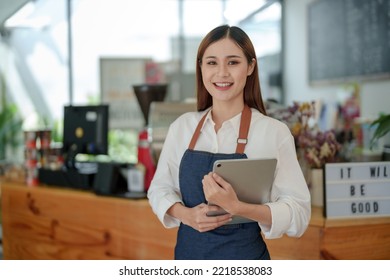 Smiling Asian woman coffee shop owner standing holding tablet and waiting for customer service with a smile.