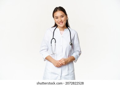 Smiling Asian Woman Doctor, Wearing Medical Robe And Stethoscope, Looking Pleasant At Patient, Standing Over White Background