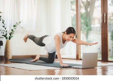 Smiling Asian Woman Doing One Arm One Leg Plank To Exercise Core Muscle Online Workout Class From Laptop At Home In Living Room. Self Isolation And Workout At Home During COVID-19.