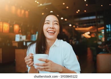 Smiling Asian woman drinking coffee in coffee shop.