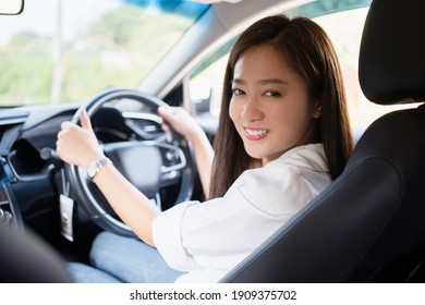 A smiling Asian woman driving to work, she is in the car.