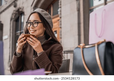 Smiling asian woman girl in eyeglasses having coffee tea hot beverage on the street outside sitting in cafe after shopping, relaxing resting alone. Traveling concept - Powered by Shutterstock