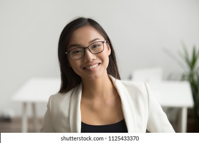 Smiling asian woman in glasses for vision correction looking at camera, happy friendly chinese student or employee posing in office, millennial japanese woman professional head shot portrait