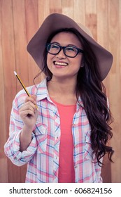 Lächelnde asiatische Frau mit Hut, die einen Bleistift auf Holzwand hält