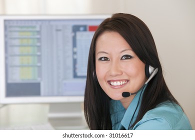 Smiling Asian Woman With Headset And Computer Monitor