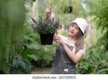 Smiling Asian Woman Holding Potted Plant Pruning Shears, Black Plant Pot Hanging In The Garden, Caring For Garden Plants For Sale, Beauty And Nature.