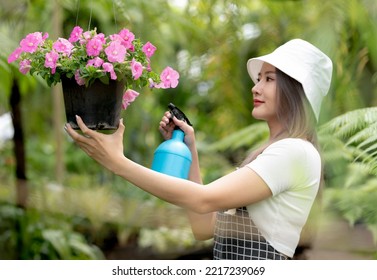 Smiling asian woman holding watering cans in pink flower pots, black plant pots hanging in the garden, garden plant care for sale, beauty and nature. - Powered by Shutterstock