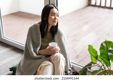 Smiling Asian Woman Looking Outside Window With Dreamy Face, Drinking Morning Coffee And Sitting Near Her Home Patio