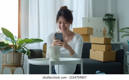 Smiling Asian Woman Online Seller Using Smart Phone Taking A Photo Of Product For Post To Sell Online On Internet.