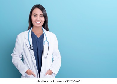 Smiling asian woman physician in a white coat over blue background