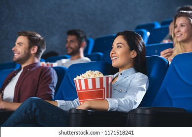 Smiling Asian Woman With Popcorn Watching Movie In Cinema Alone