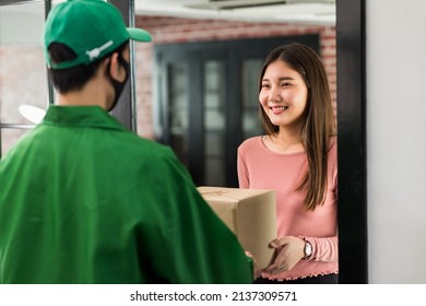 Smiling Asian Woman Receive Delivery Parcel From Courier Man With Face Mask At Door Inside Apartment Or Condo. New Normal To Order Goods Online By Application During Covid-19 Omicron Pandemic..