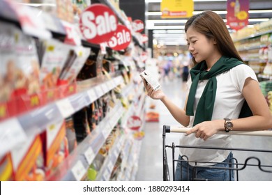 Smiling Asian woman shopping in a supermarket and reading product information.