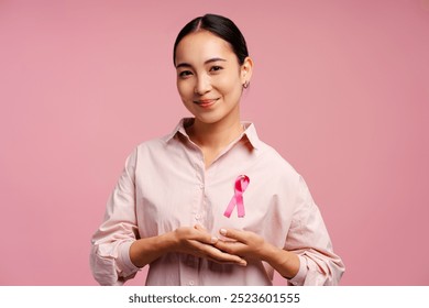 Smiling Asian woman smiling and showing pink ribbon for breast cancer awareness on pink background. Breast cancer awareness concept - Powered by Shutterstock