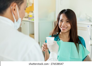 Smiling Asian Woman Is Taking A Glass Of Water From Her Dentist