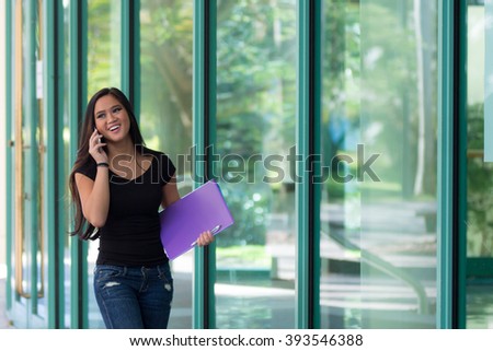 Smiling Asian woman talks on cell phone while walking next to glass building