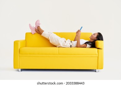Smiling asian woman types text message on cell phone, enjoys online communication lying on yellow couch on white background. Technology, communication concept - Shutterstock ID 2033388443
