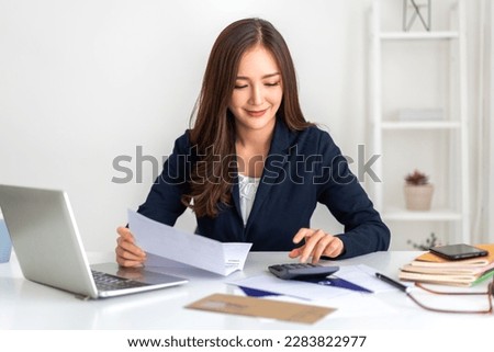 Smiling asian woman using calculator and calculate bills on laptop, paying bill, credit card, finance, tax, vat, credit card,  payment, tax refund, budget, debt, money.financial and accounting concept