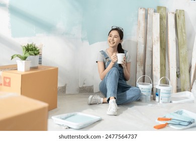 Smiling asian woman using phone after painting in room at new home.Asian young woman resting with coffee after work concept of paint color,moving house,decorating house,new house. - Powered by Shutterstock