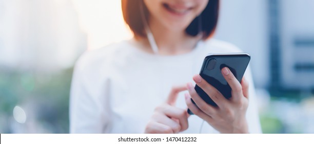 Smiling Asian Woman Using Smartphone With Listening To Music And Standing In Office Building.