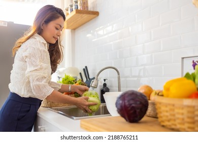 Smiling Asian Woman Washing Vegetables In Kitchen Sink For Cooking And Making Salad In The Kitchen At Home. Attractive Woman Vegetarian Enjoy Cooking And Eating Healthy Food On Summer Holiday Vacation