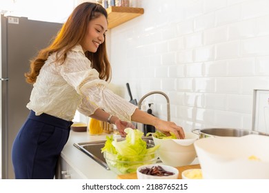 Smiling Asian Woman Washing Vegetables In Kitchen Sink For Cooking And Making Salad In The Kitchen At Home. Attractive Woman Vegetarian Enjoy Cooking And Eating Healthy Food On Summer Holiday Vacation