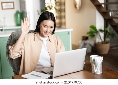 Smiling asian woman waving hello at video chat on laptop, sitting at home, studying remotely in e-learning school