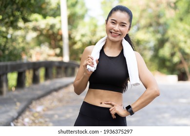 Smiling Asian Woman Wearing Black Sportswear And Sweat Wipes On Neck And Exercising Outdoor. Healthy And Sport Concept.